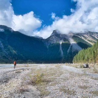 Male hiker trekking through Kinney Flats in shadow of imposing mountain on Berg Lake Trail in Mount Robson Provincial Park