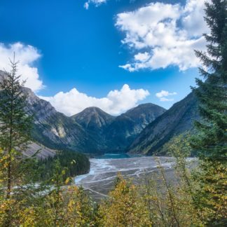 Edge of Kinney Lake in distance encapsulated by mountains on Berg Lake Trail in Mount Robson Provincial Park on sunny day