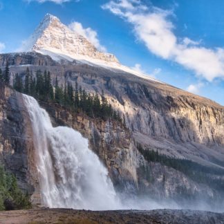 Emperor Falls beneath Mount Robson under sunny blue skies with mist from waterfall drifting to the right