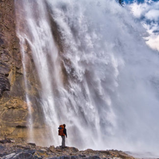 Male hiker standing in awe at close-up of Emperor Falls on sunny day in Mount Robson Provincial Park