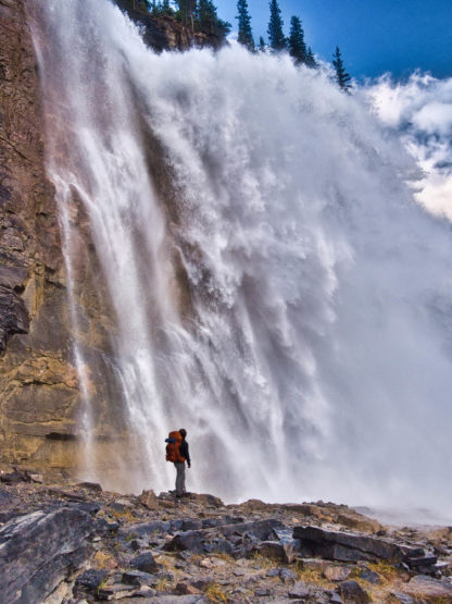 Male hiker standing in awe at close-up of Emperor Falls on sunny day in Mount Robson Provincial Park