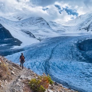 Male hiker walks around switchback in Snowbird Pass in front of Robson Glacier in Mount Robson Provincial Park on cloudy day