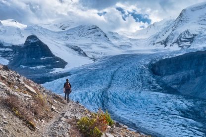 Male hiker walks around switchback in Snowbird Pass in front of Robson Glacier in Mount Robson Provincial Park on cloudy day